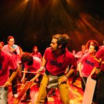 A group of students perform on drums wearing red t-shirts