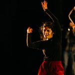 A student wearing a black top and red trousers dances on stage
