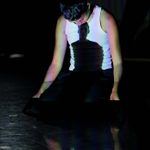 A dancer wearing a white top performs with shadows projected onto their body