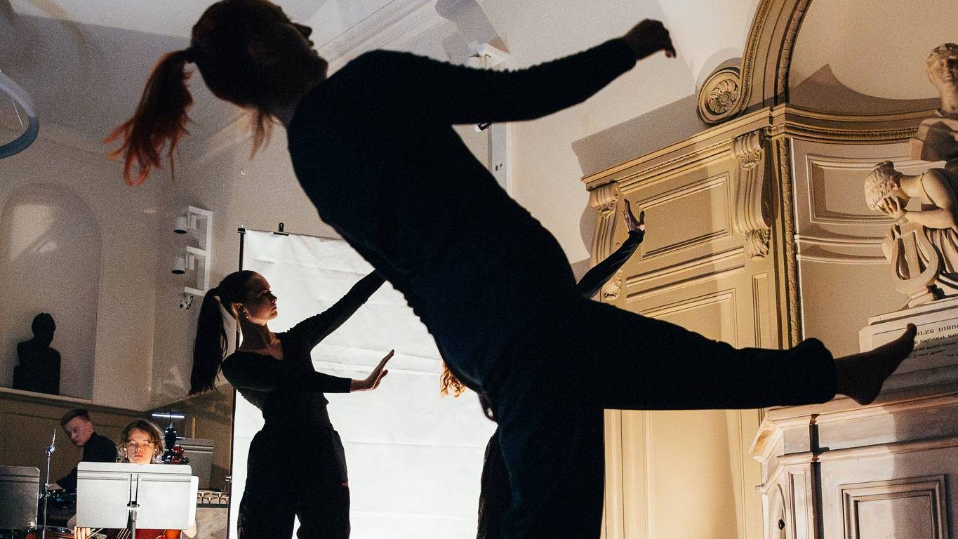 Two dancers are in silhouette with musicians performing as they move