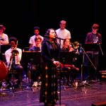 A singer performs at a microphone with a band in the background