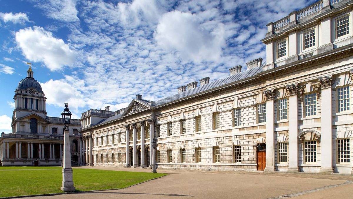 Trinity Laban's King Charles Court building in Greenwich. The building is white stone, and there is a green lawn in front of it.