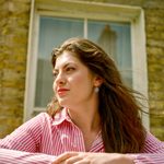 A musical theatre student with long hair and a striped dress stands in front of a window